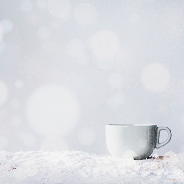 Cup on bank of snow and snowflakes