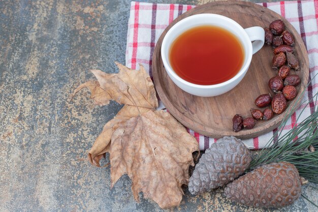 Tazza di tè nero e rosa canina essiccata sul piatto di legno con pigne nelle quali. foto di alta qualità