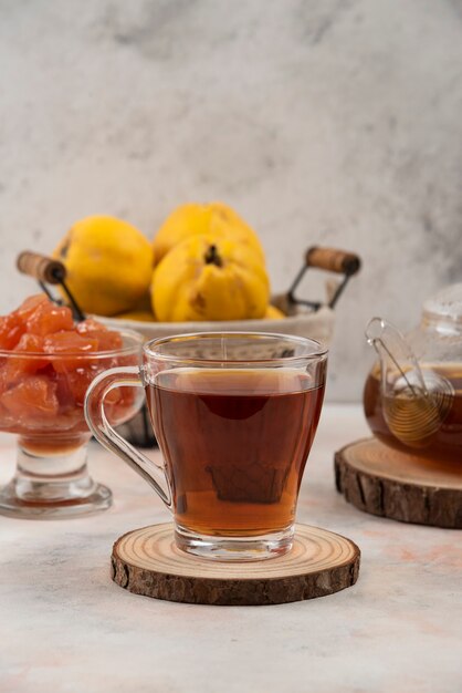 Cup of black tea, quince fruit and jam on marble table. 