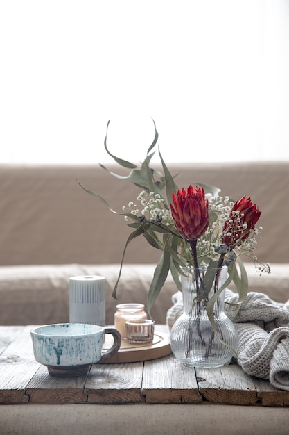 Cup, candles, vase with protea flowers and a knitted element in the room on a blurred background.