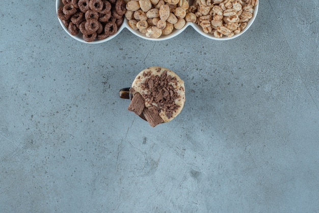 A cup of cappuccino next to cornflakes in a bowls , on the blue background.