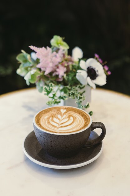 Cup of cappuccino on saucer beside flower centerpiece