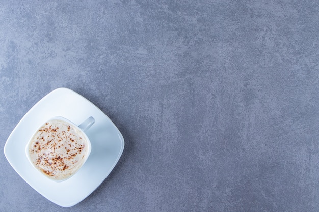 A cup of cappuccino on a saucer, on the blue table.