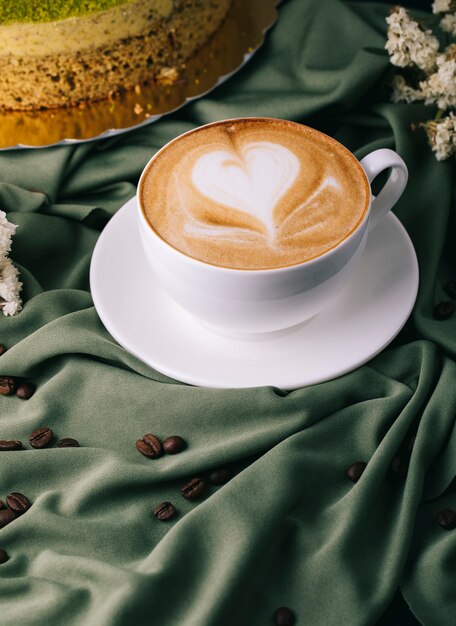 Cup of cappuccino with coffee beans and cake on the table