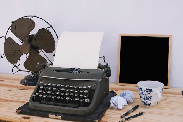 Cup and chalkboard near typewriter and fan