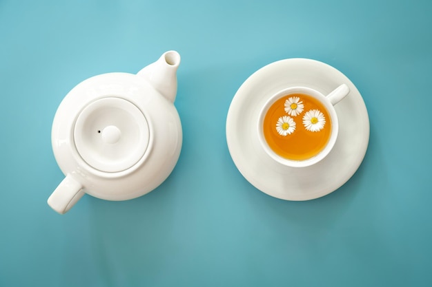 A cup of chamomile tea and a teapot on a blue background