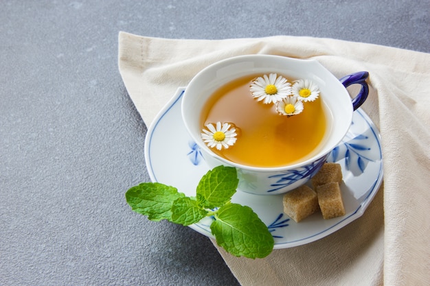 Free photo a cup of chamomile tea with sugar cubes, leaves high angle view on a cloth