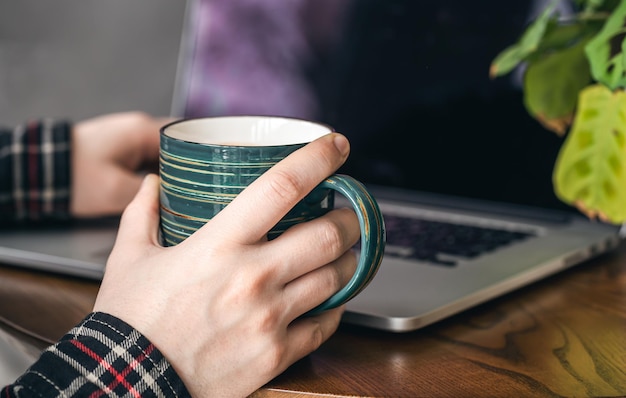 Free photo a cup of cocoa in male hands on the background of a laptop