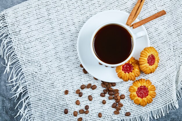 A cup of coffee, biscuits, coffee beans and cinnamon.