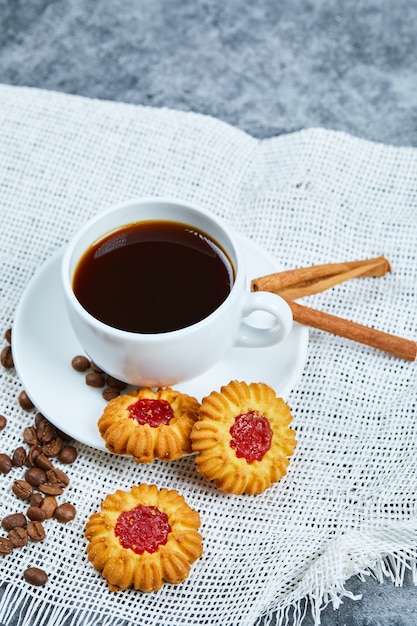 A cup of coffee, biscuits, coffee beans and cinnamon.