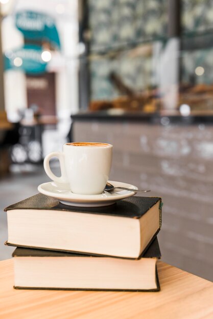 Cup of coffee over books on wooden table