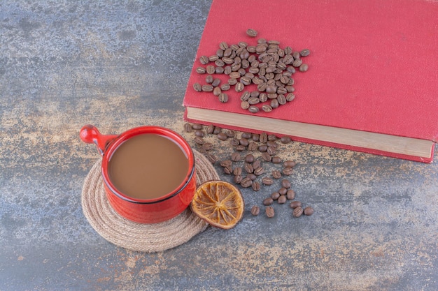 Cup of coffee, coffee beans and book on marble surface. High quality photo