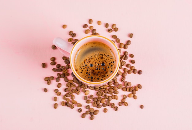 Cup of coffee and coffee beans on pink surface