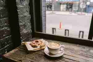 Free photo cup of coffee next to a cookie put on the windowsill