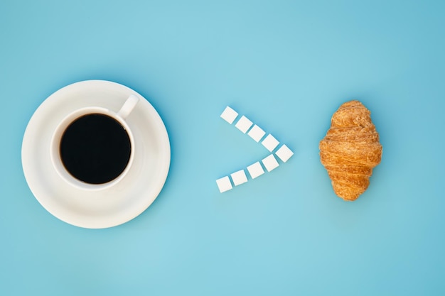 A cup of coffee and a croissant on blue background flat lay