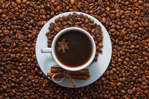 A cup of coffee and dry cinnamon with coffee beans on background. top view.