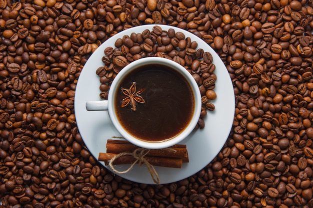 一杯のコーヒーと背景にコーヒー豆と乾燥シナモン。上面図。
