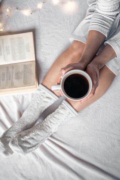 Cup of coffee in female hands in bed top view