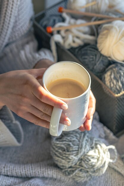 A cup of coffee in female hands and a thread of yarn