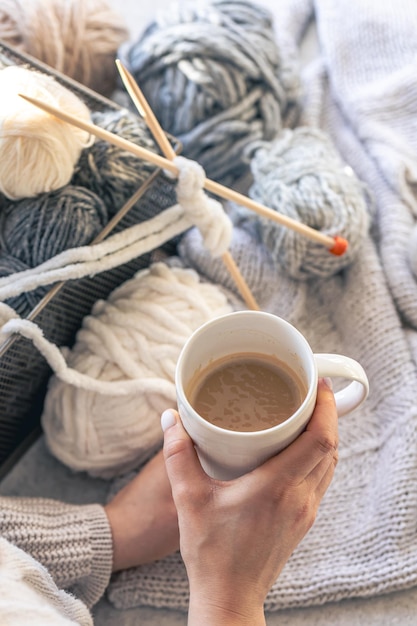 A cup of coffee in female hands and a thread of yarn