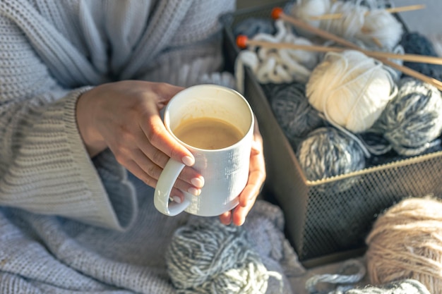 A cup of coffee in female hands and a thread of yarn