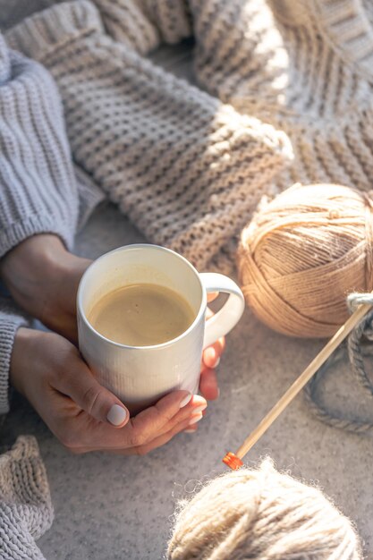 A cup of coffee in female hands and a thread of yarn