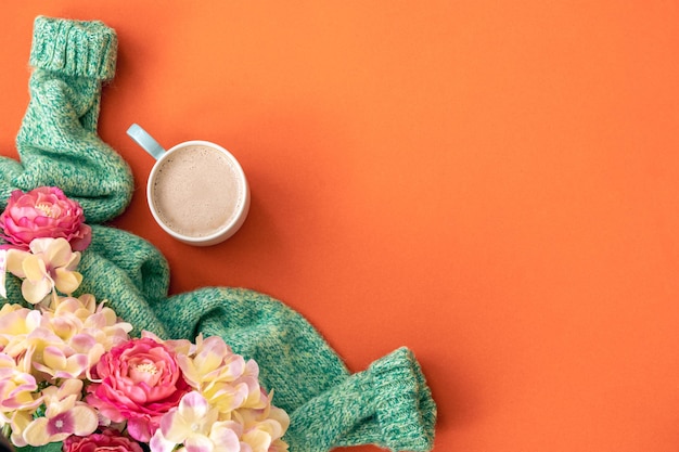 Cup of coffee flowers and knitted element on orange background flat lay