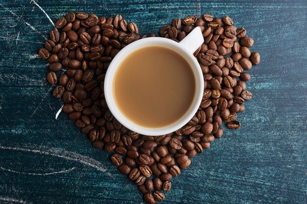 A cup of coffee on grains in heart shape.