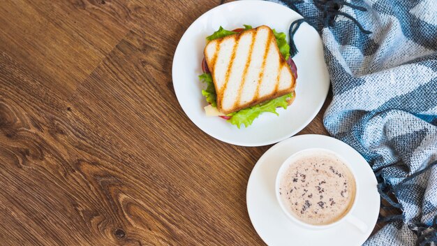 Cup of coffee and grilled sandwich with napkin on wooden table