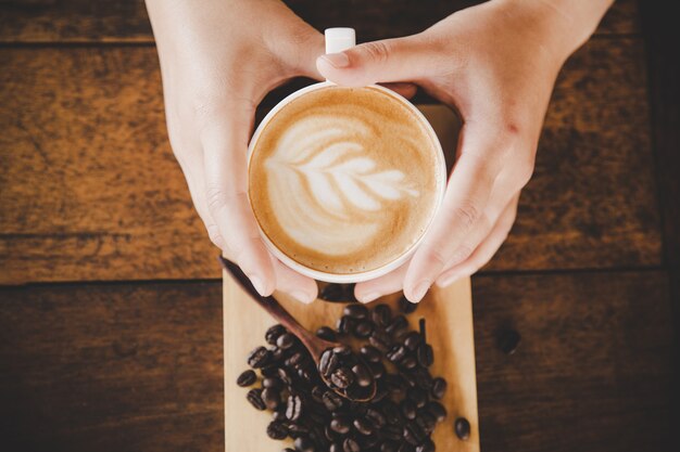 A cup of coffee in hand of women on wood texture. 