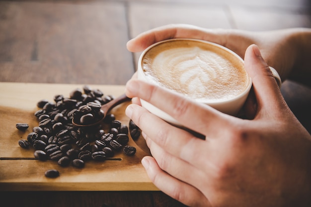 A cup of coffee in hand of women on wood texture. 