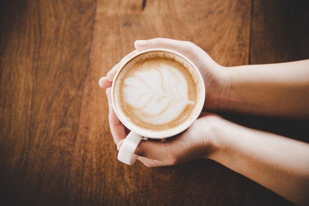 Чашка кофе в руке женщин на деревянной текстуре.