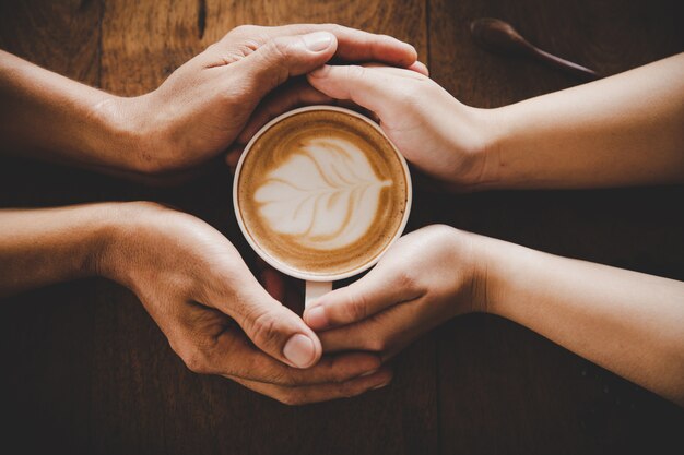 A cup of coffee in the hands of a man and a woman. Selective focus.