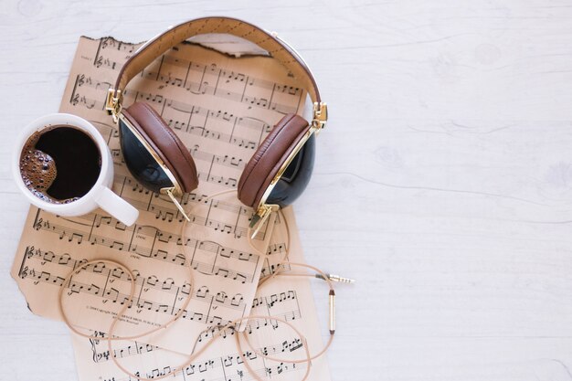 Cup of coffee and headphones near sheet music