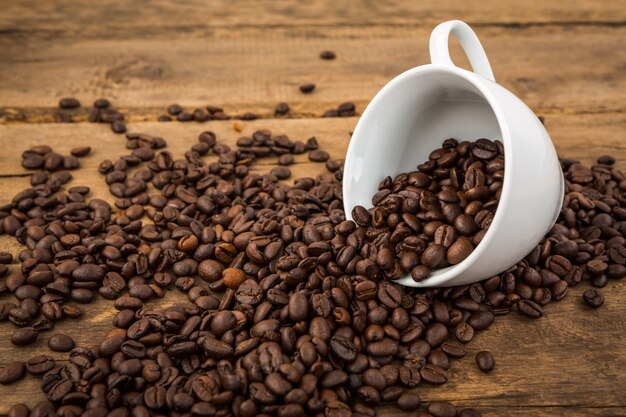 Чашка кофе, лежа с кофе в зернах выходит из него