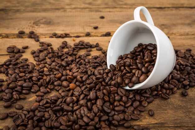 Cup of coffee lying down with coffee beans coming out of it