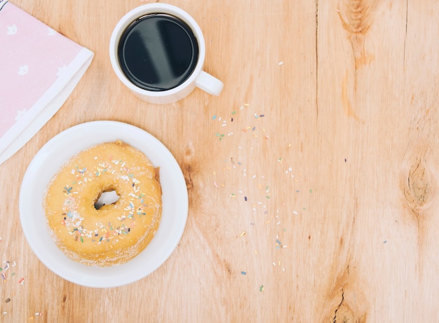Cup of coffee; napkin and fresh baked donut on plate over wooden background
