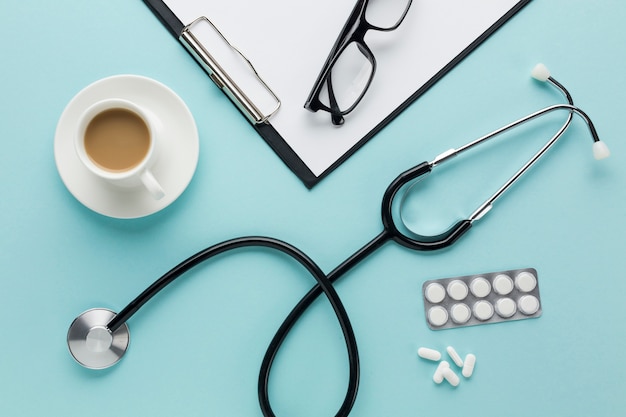 Cup of coffee near spectacles on clipboard with doctor's accessories on background