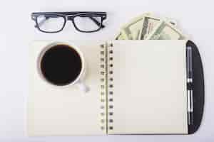 Free photo cup of coffee on notebook with glasses on desk