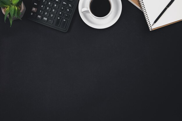 Free photo a cup of coffee notepads a calculator on a black background top view