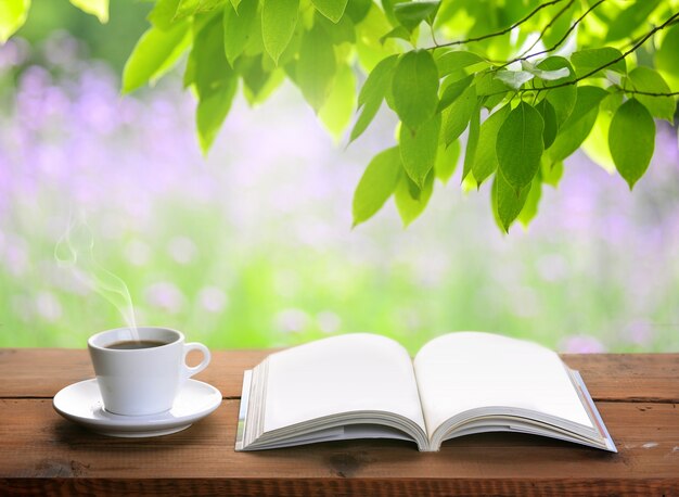 Cup of coffee and open book on wooden table