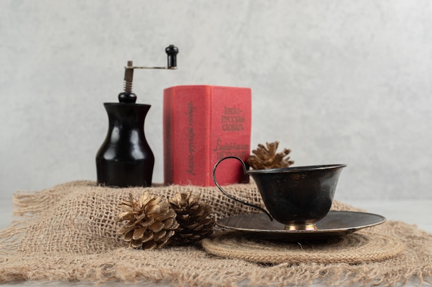 Cup of coffee, pinecones and book on burlap