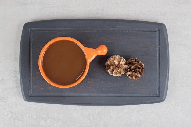 Cup of coffee and pinecones on dark plate