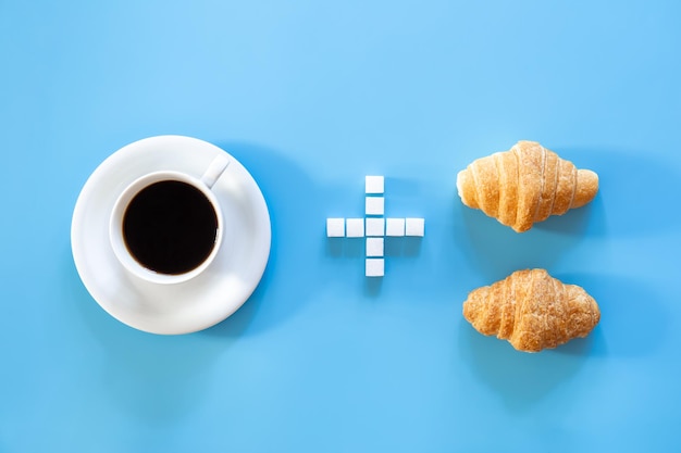 Una tazza di caffè un segno più fatto di zucchero e un croissant piatto