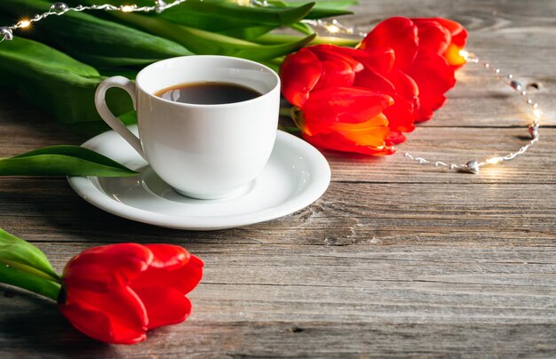 Free photo cup of coffee and red tulips on a wooden surface