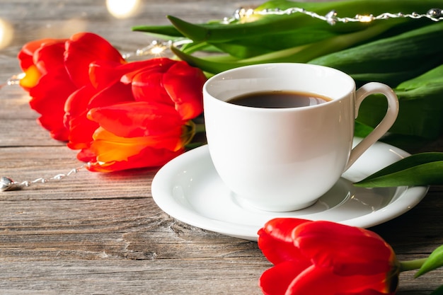 Cup of coffee and red tulips on a wooden surface