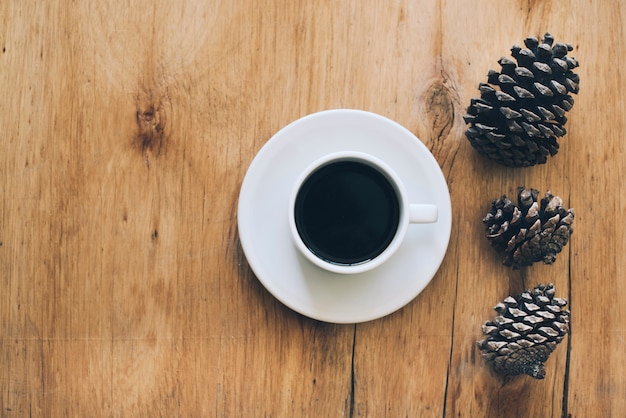 Cup of coffee and saucer with three pinecones on wooden textured backdrop