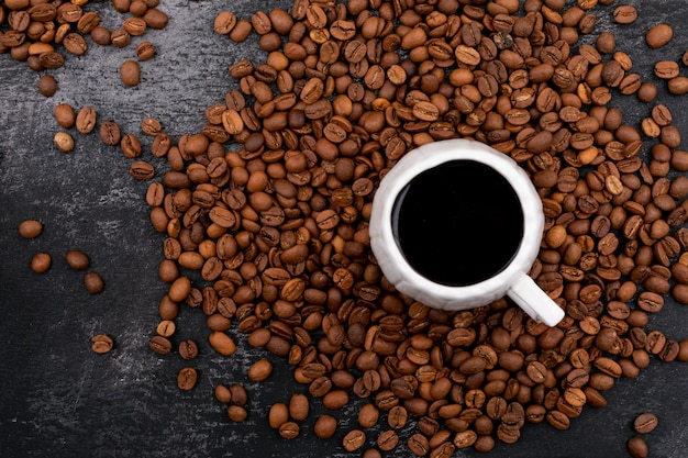 Cup of coffee surrounded with coffee beans on black surface