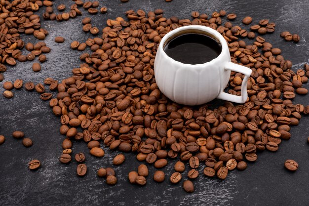 Чашка кофе в окружении кофейных зерен на черной поверхности