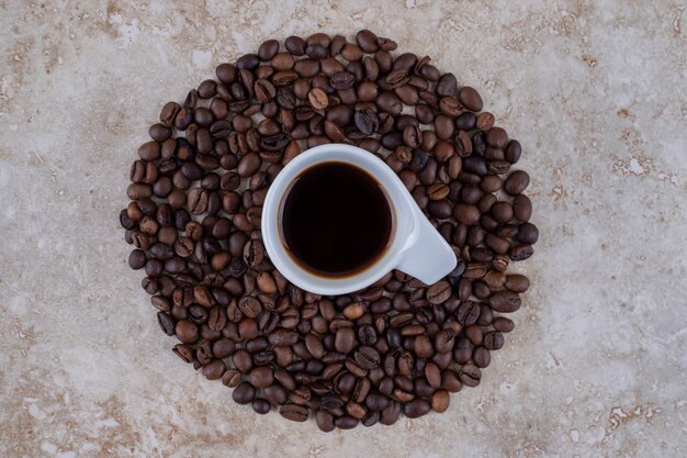 A cup of coffee surrounded with coffee beans 